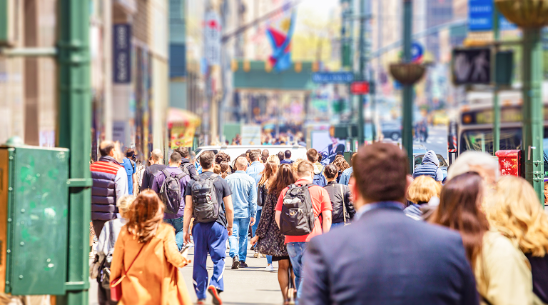 A large group of pedestrians walking along a city avenue lined with tall buildings