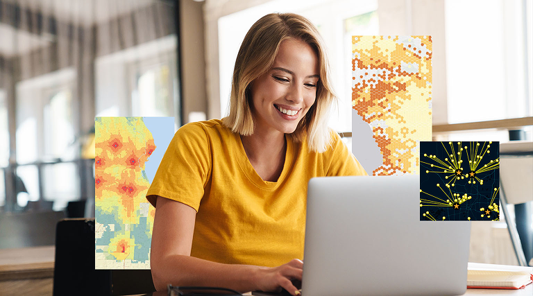 A woman in a yellow shirt is seated at a desk, working on a laptop.
