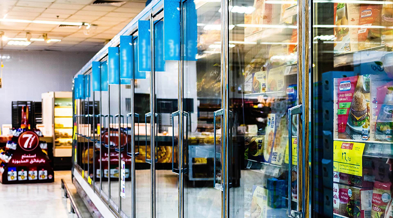 Glass-door refrigerator cases stocked with products along a grocery store aisle